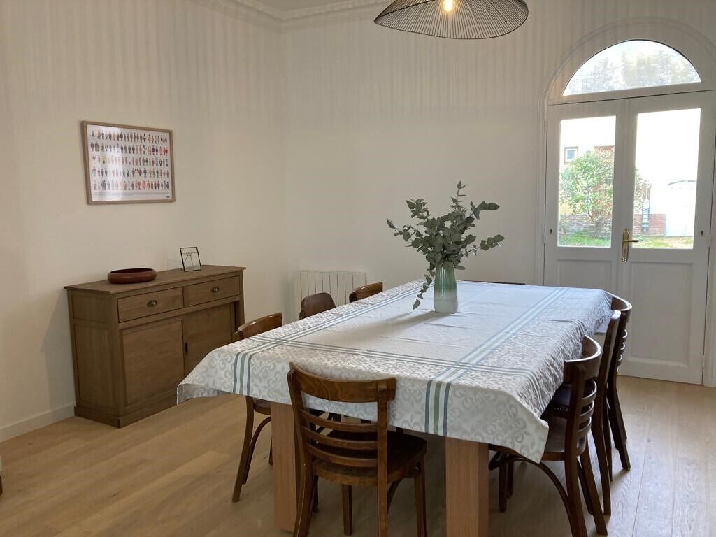A dining area with a table set for four, a vase with flowers, and a wooden cabinet.