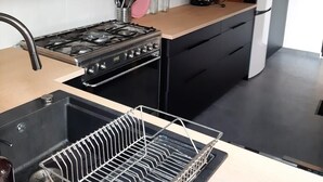 A modern kitchen with a black stove, a sink with a dish rack, and a wooden countertop.