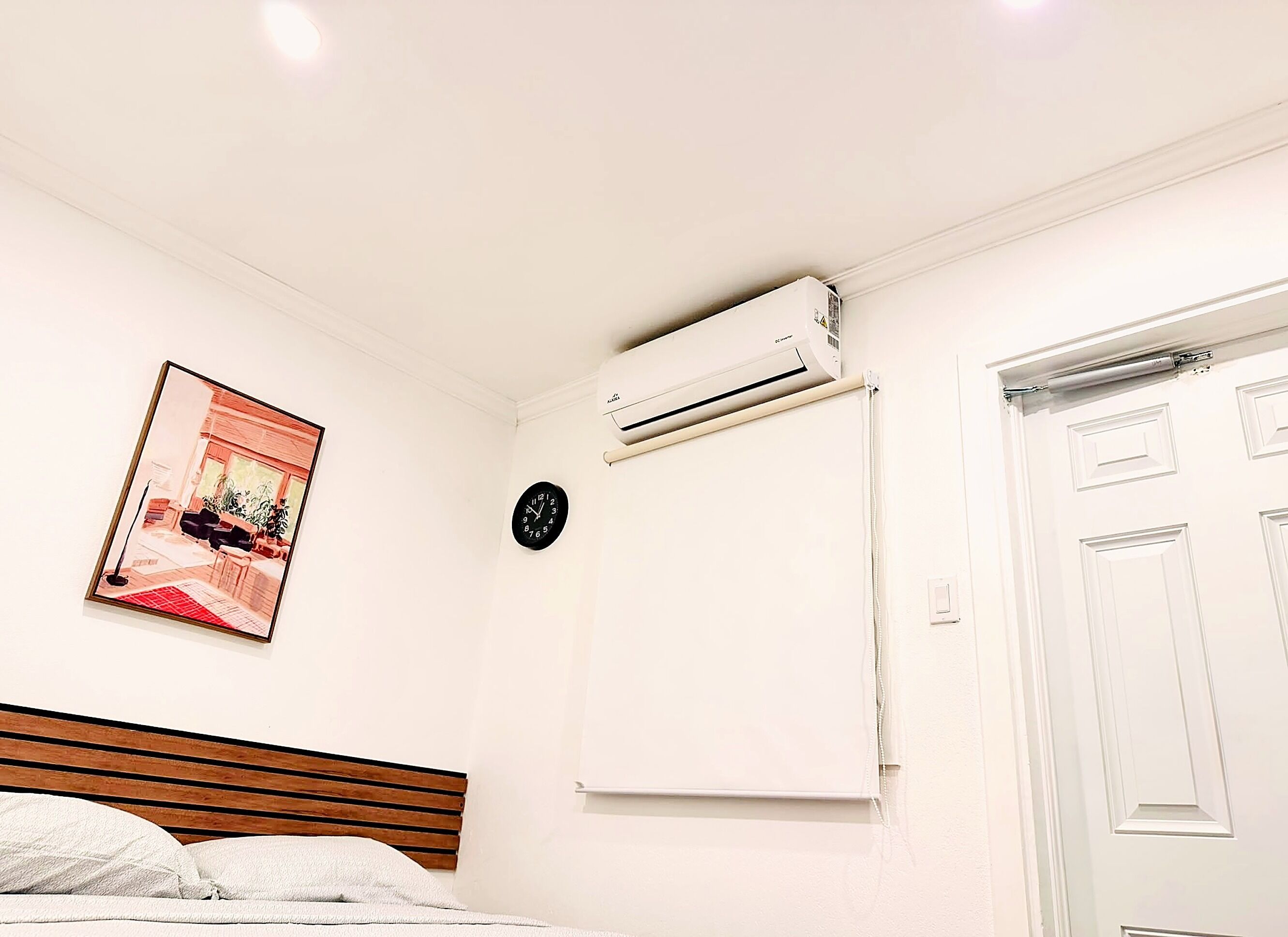 Un dormitorio con cama, aire acondicionado, un reloj y una puerta.