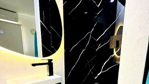 A bathroom with a modern design, featuring a white sink, a black cabinet, and a marble-patterned wall. - Room-hideaway Layover #20 - by Zenbreak (Oistins)