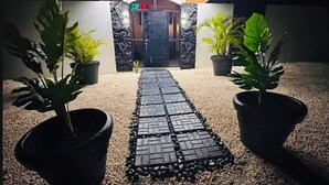 Un camino que lleva a la entrada de un edificio, con una señal que dice 'OPEN', flanqueado por macetas con plantas.