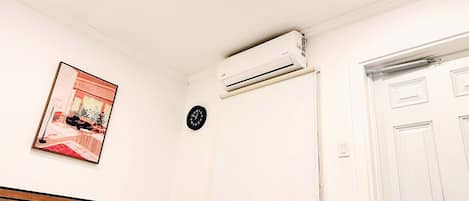 A bedroom with a bed, an air conditioning unit, a clock, and a door.