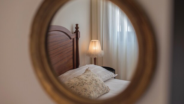 Un dormitorio con cabecera de madera, lámpara de noche, almohada y ventana con cortinas.