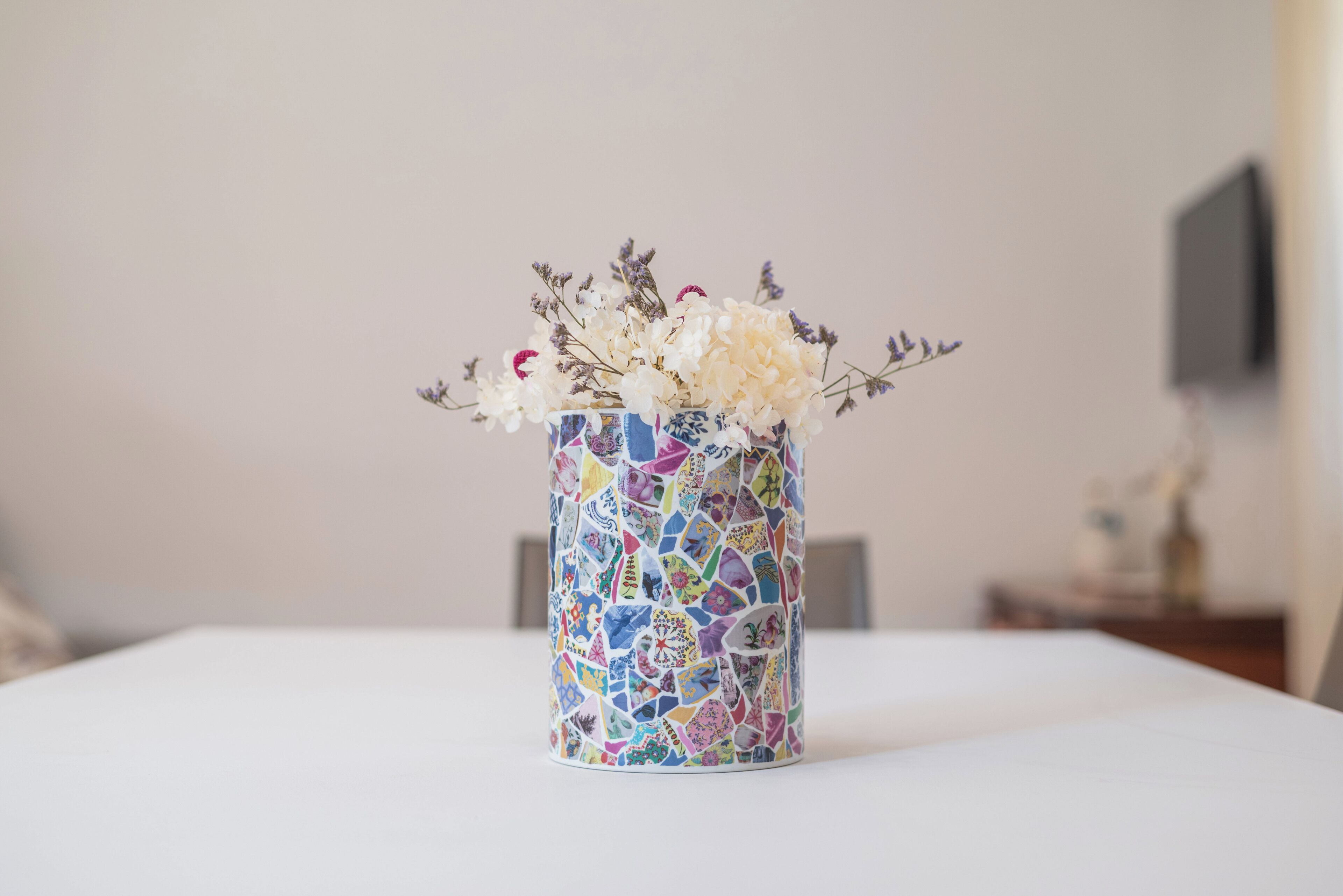 A vase with a mosaic pattern containing flowers and dried plants.
