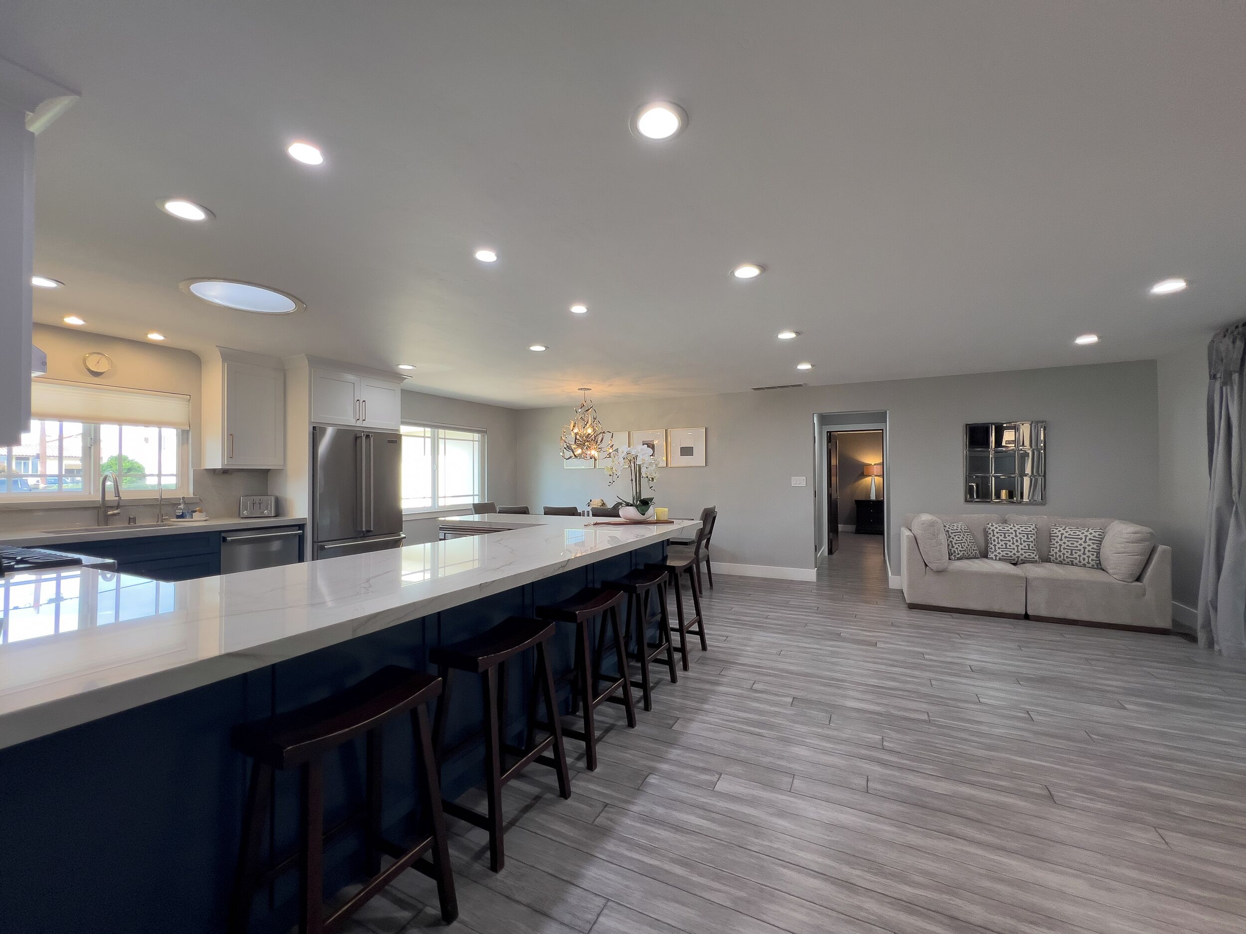 A modern kitchen with a central island, bar stools, and a dining area with a sofa.