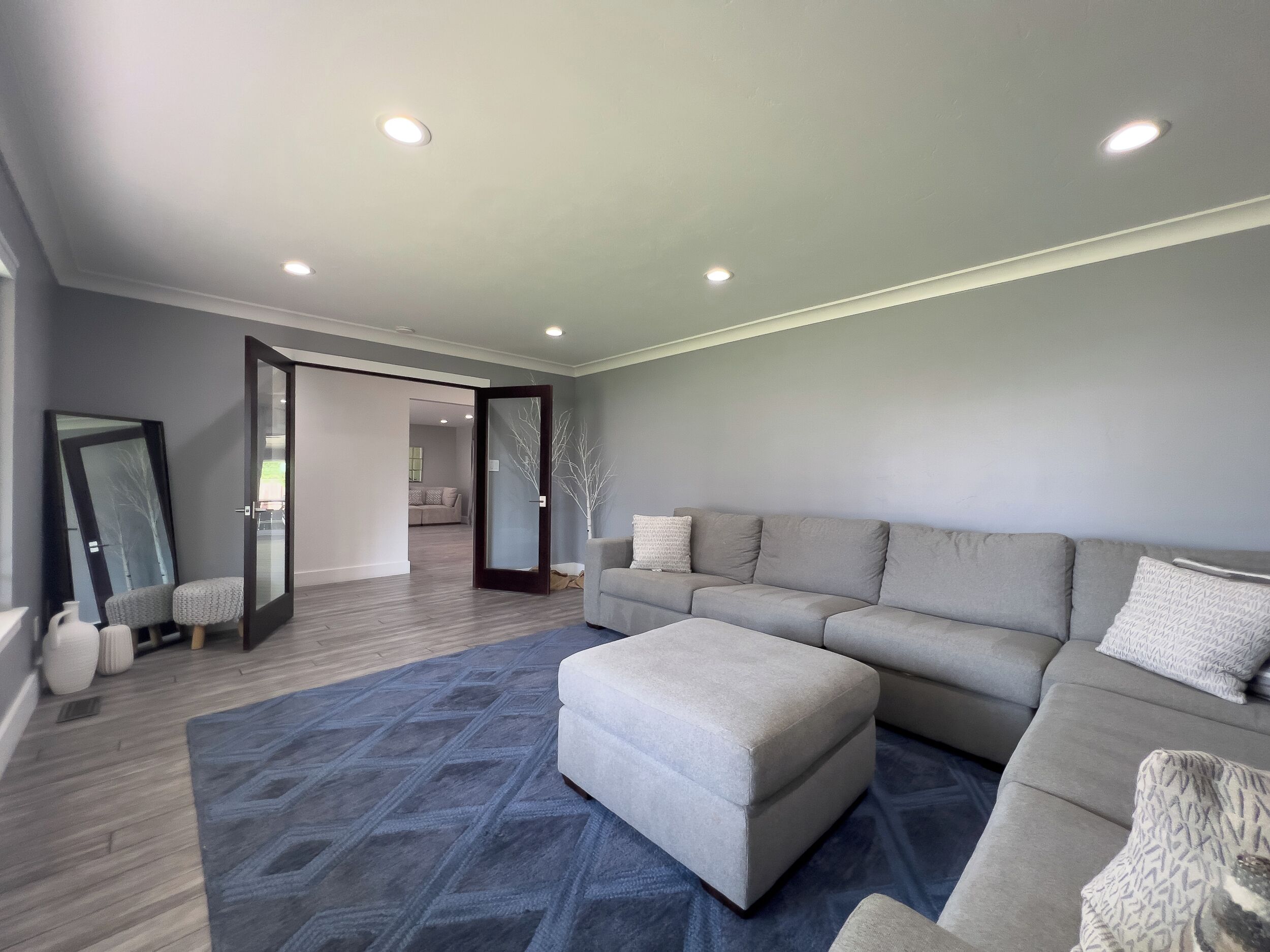 A modern living room with a grey sofa, ottoman, and a patterned rug.
