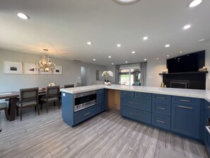 Una cocina moderna con una isla grande, electrodomésticos integrados y un comedor con candelabro.
