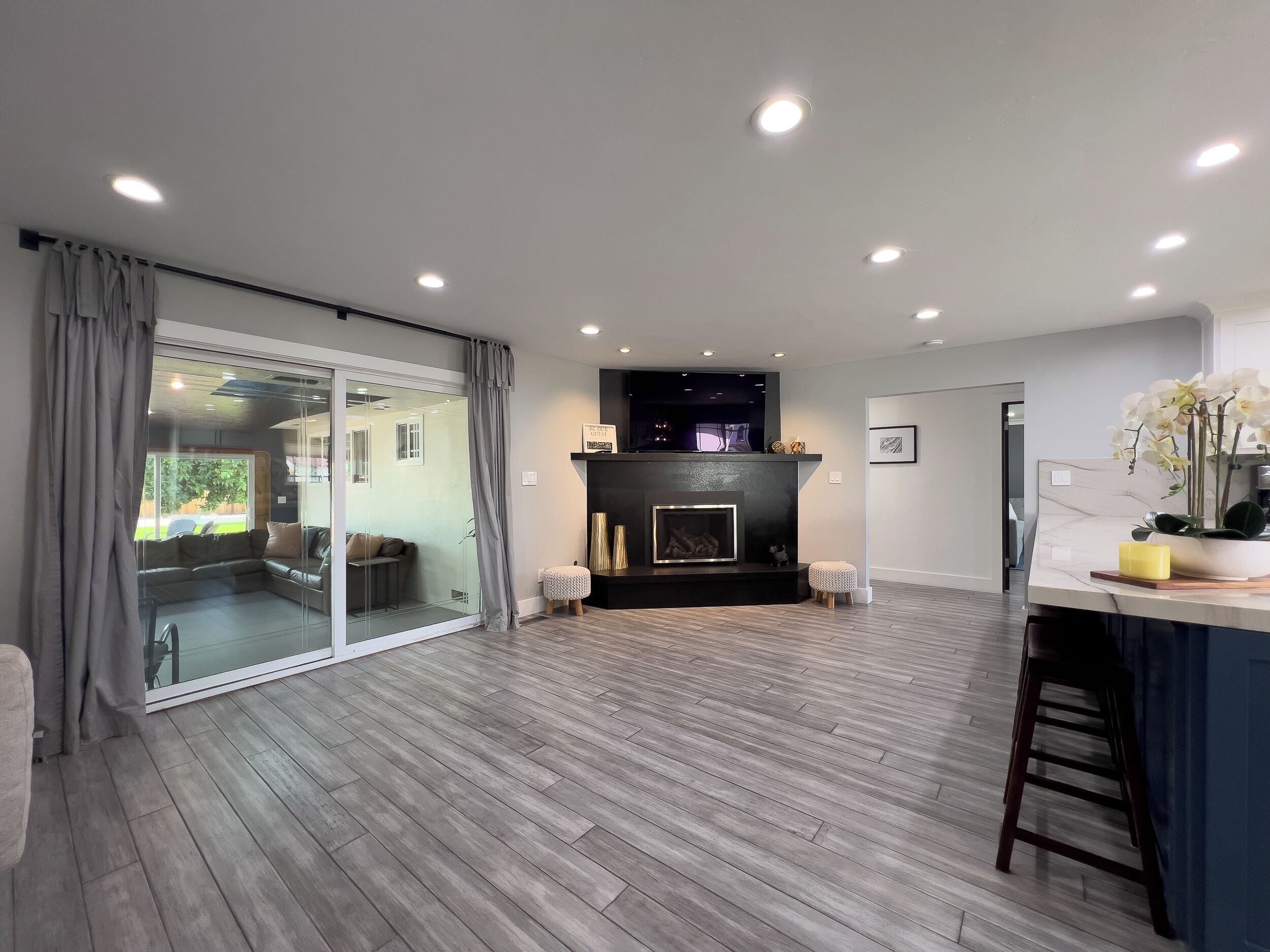 A modern living room with a fireplace, a glass sliding door leading to a balcony, and a marble countertop with a vase of flowers.