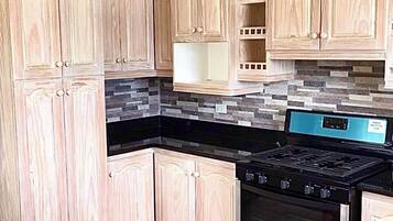 A kitchen with wooden cabinets, a black countertop, and a stainless steel stove.