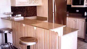 Eine Küche mit Holzausstattung, einem Edelstahlkühlschrank, Granit Arbeitsplatten und zwei Barhocker.