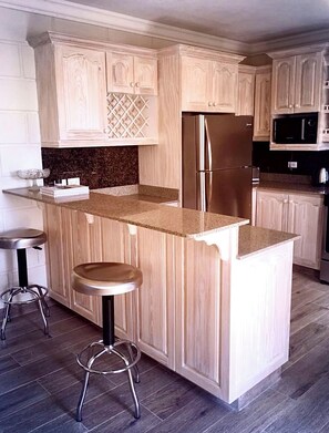 Eine Küche mit Holzausstattung, einem Edelstahlkühlschrank, Granit Arbeitsplatten und zwei Barhocker.