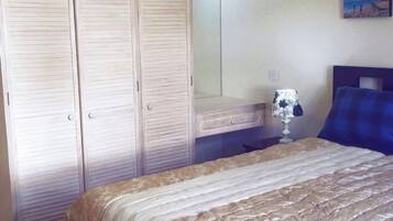 Un dormitorio con cama, mesita de noche, lámpara y armario.