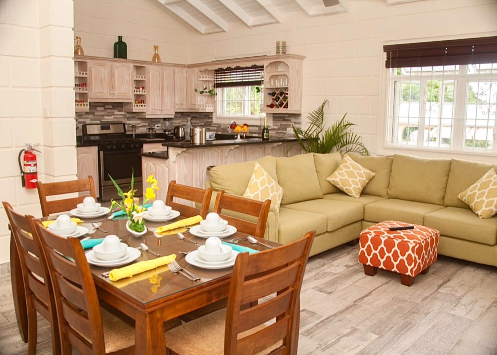 A dining area with a table set for four, a sofa, and a window with blinds.