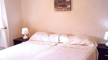 Un dormitorio con cama, dos mesitas de noche con lámparas, aire acondicionado en la pared y un cuadro enmarcado.