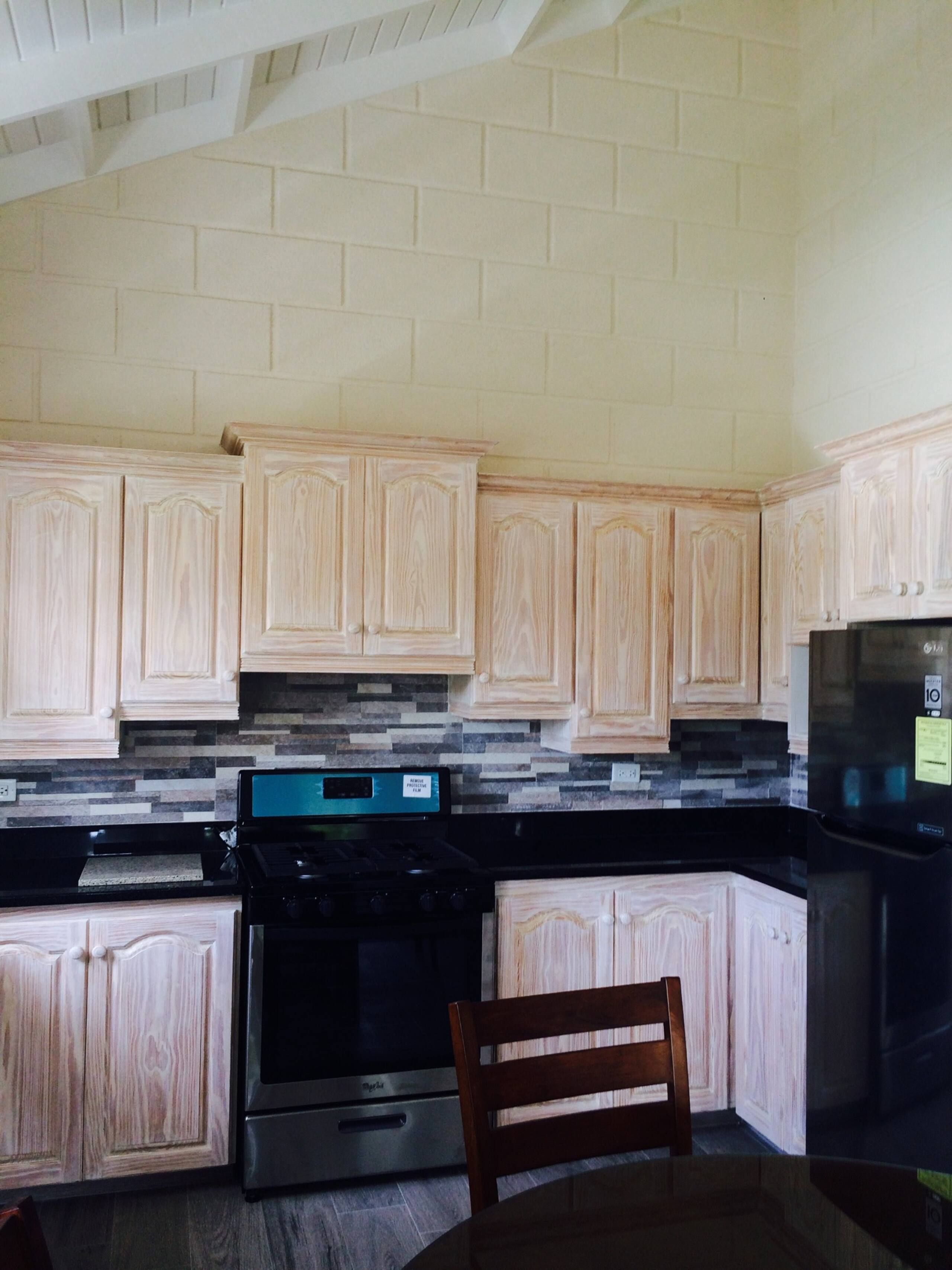 A kitchen with light wood cabinets, a black countertop, a stainless steel stove, and a black refrigerator.