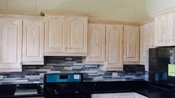 Una cocina con armarios de madera clara, encimera negra, estufa de acero inoxidable y refrigerador negro.