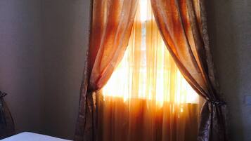 Una habitación con cama, ventana con cortinas y techo con vigas.
