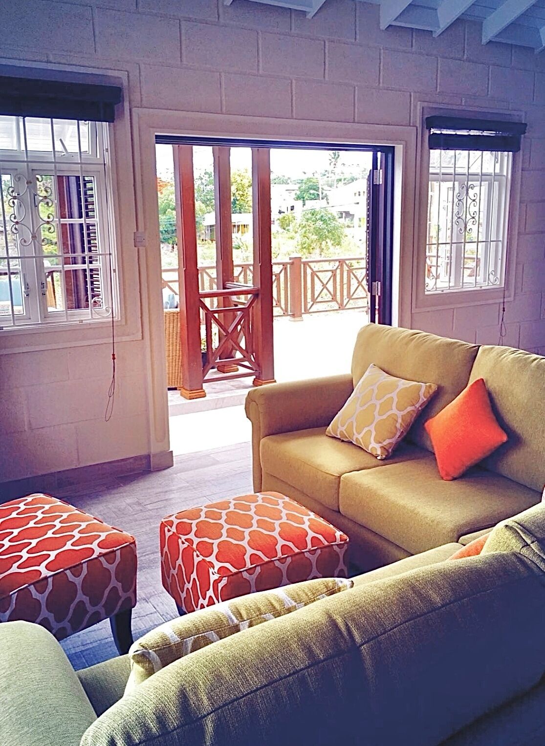 A living room with a sofa, ottomans, and a view through a glass door to an outdoor area.