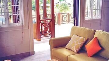 A living room with a sofa, ottomans, and a view through a glass door to an outdoor area.