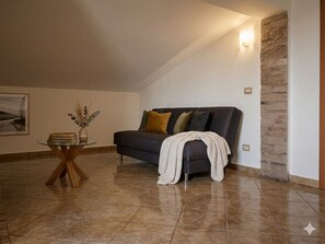 A living room with a dark-colored sofa, a glass coffee table, and a stone accent wall. - Romantic Attic Room with Ocean View for Couples (Porto Torres)