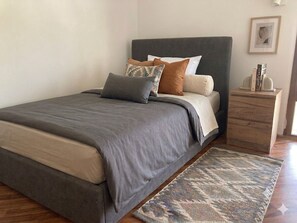 A bed with a grey headboard, multiple pillows, and a patterned rug. - Romantic Attic Room with Ocean View for Couples (Porto Torres)