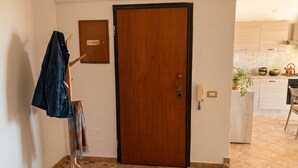 A hotel room with a wooden door, a coat rack with a jacket, a small plant, and a tiled floor.