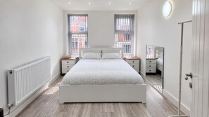 A bedroom with a white bed, two nightstands, a radiator, and a large window with blinds. - Cardiff 5-bed House, Sleeps 13 w/ Parking & Garden (Cardiff)