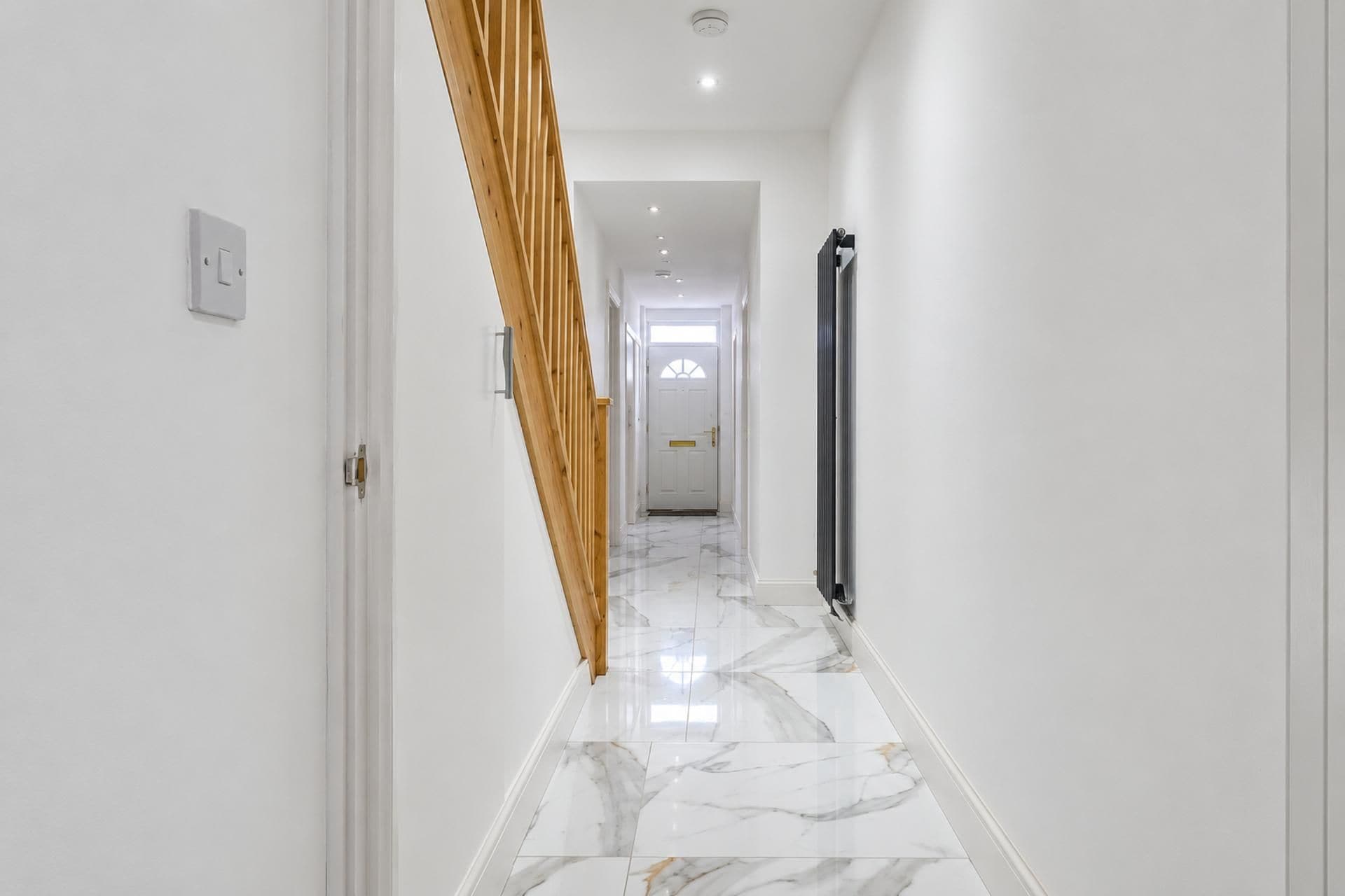 A hallway with a marble floor, a wooden staircase, and a radiator.