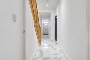 Um corredor com piso de mármore, escada de madeira e radiador.