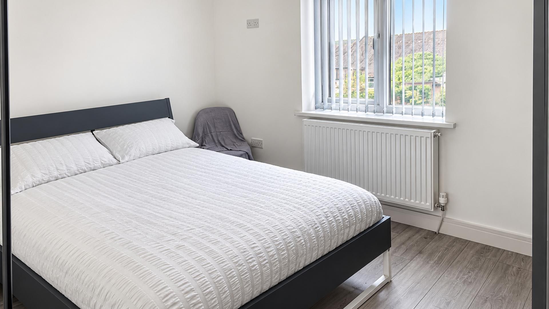A bedroom with a bed, a radiator, a window, and a chair.