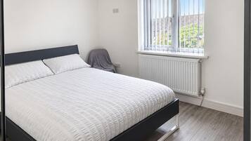 A bedroom with a bed, a radiator, a window, and a chair.