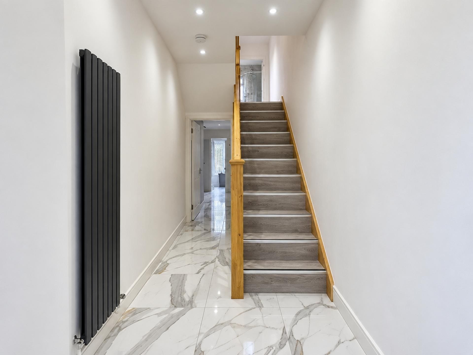 A modern interior with a marble floor, a wooden staircase, and a radiator.