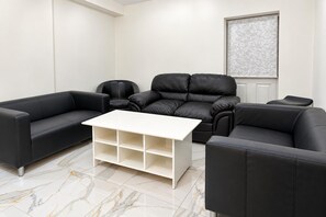 A modern living room with a black leather sofa, a white coffee table, and a marble-tiled floor. - Cardiff 5-bed House, Sleeps 13 w/ Parking & Garden (Cardiff)