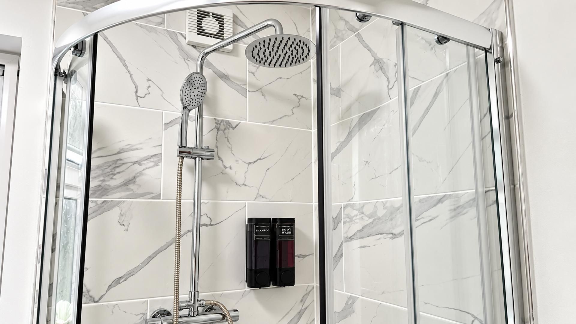 A shower enclosure with a handheld showerhead and a rain showerhead, a handheld shower attachment, and two bottles of shampoo and body wash.