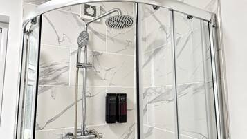 A shower enclosure with a handheld showerhead and a rain showerhead, a handheld shower attachment, and two bottles of shampoo and body wash.