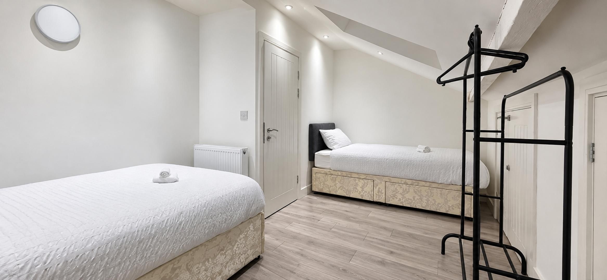 A bedroom with two beds, a radiator, and a black metal rack.