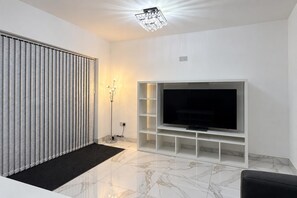 A modern living room with a flat-screen TV, a radiator, a floor lamp, and a marble floor. - Cardiff 5-bed House, Sleeps 13 w/ Parking & Garden (Cardiff)