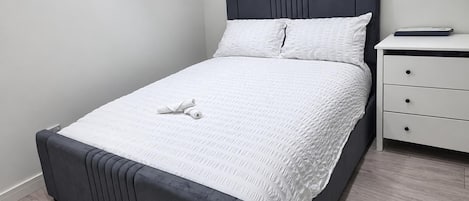 Una cama con cabecera oscura, ropa de cama blanca y almohada blanca.
