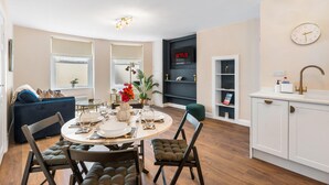 Eine moderne Küche mit integriertem Geschirrspüler, ein Essbereich mit rundem Tisch und Stühlen sowie ein Wohnbereich mit Sofa und Fernseher.