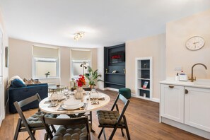 Eine moderne Küche mit integriertem Geschirrspüler, ein Essbereich mit rundem Tisch und Stühlen sowie ein Wohnbereich mit Sofa und Fernseher.