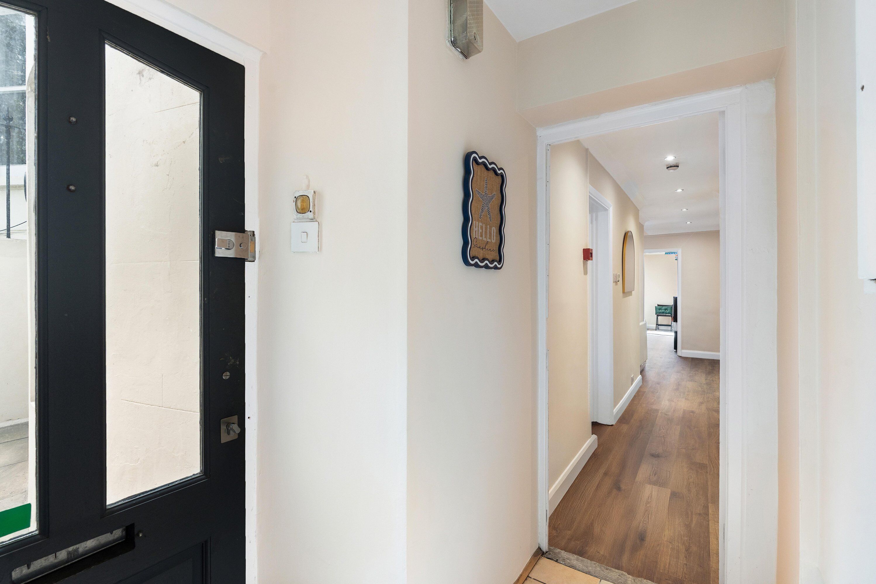 A hallway with a black door, a wall-mounted light switch, and a decorative starfish sign.