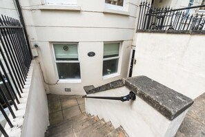A staircase with a handrail, a window, and a door with a number plate. - Coastal Calm | By My Getaways (Brighton)