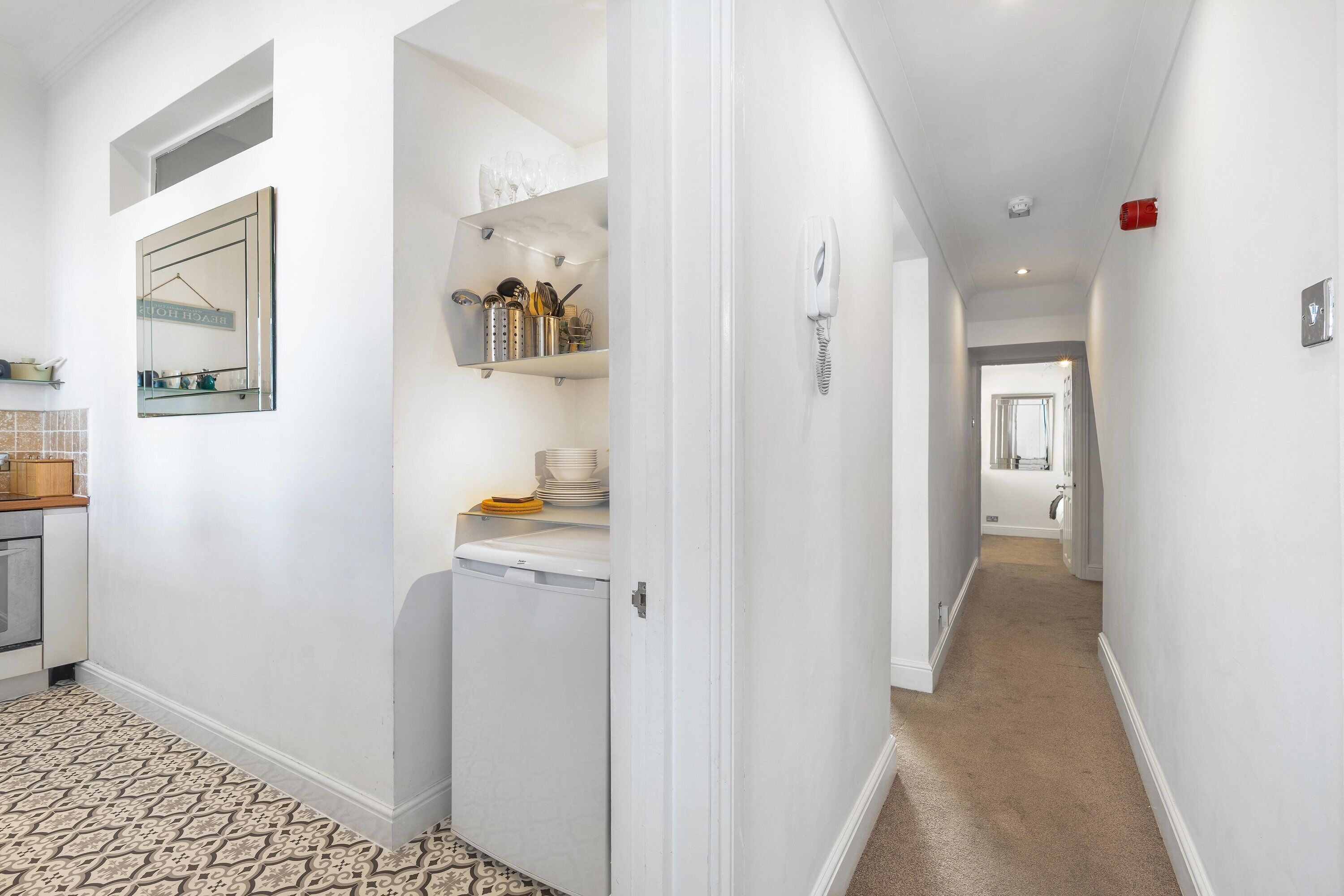A hallway with a kitchen area on the left, a white washing machine, and a door leading to another room.