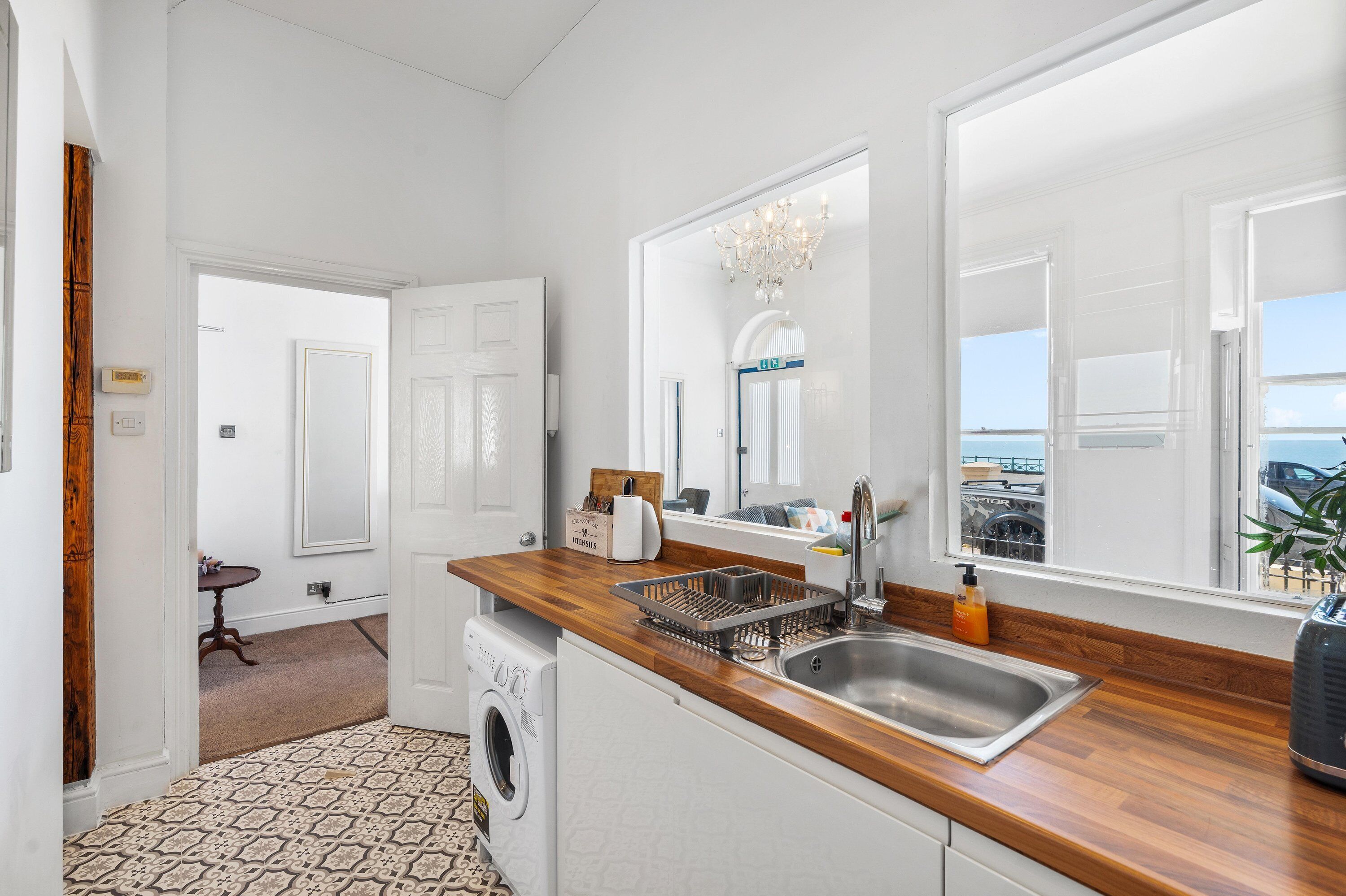 A compact kitchen with a washing machine, a sink, and a window with a view of the sea.