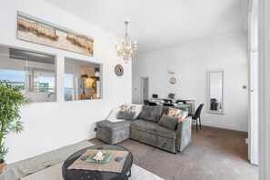 A modern living room with a sectional sofa, a dining area, and a view of the outdoors. - Seaview Haven | By My Getaways (Brighton)