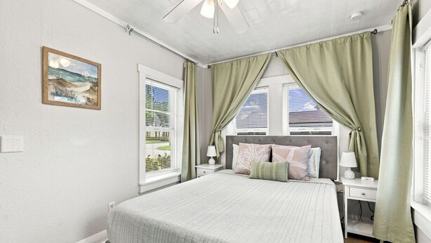 Um quarto com uma cama, uma mesa de cabeceira, um abajur, um quadro e uma janela com cortinas.