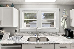 A kitchen with a double sink, white cabinets, a window with blinds, and a small sailboat decoration. - 2 bed 2 bath Home Close to Downtown and Stadiums (Tampa)
