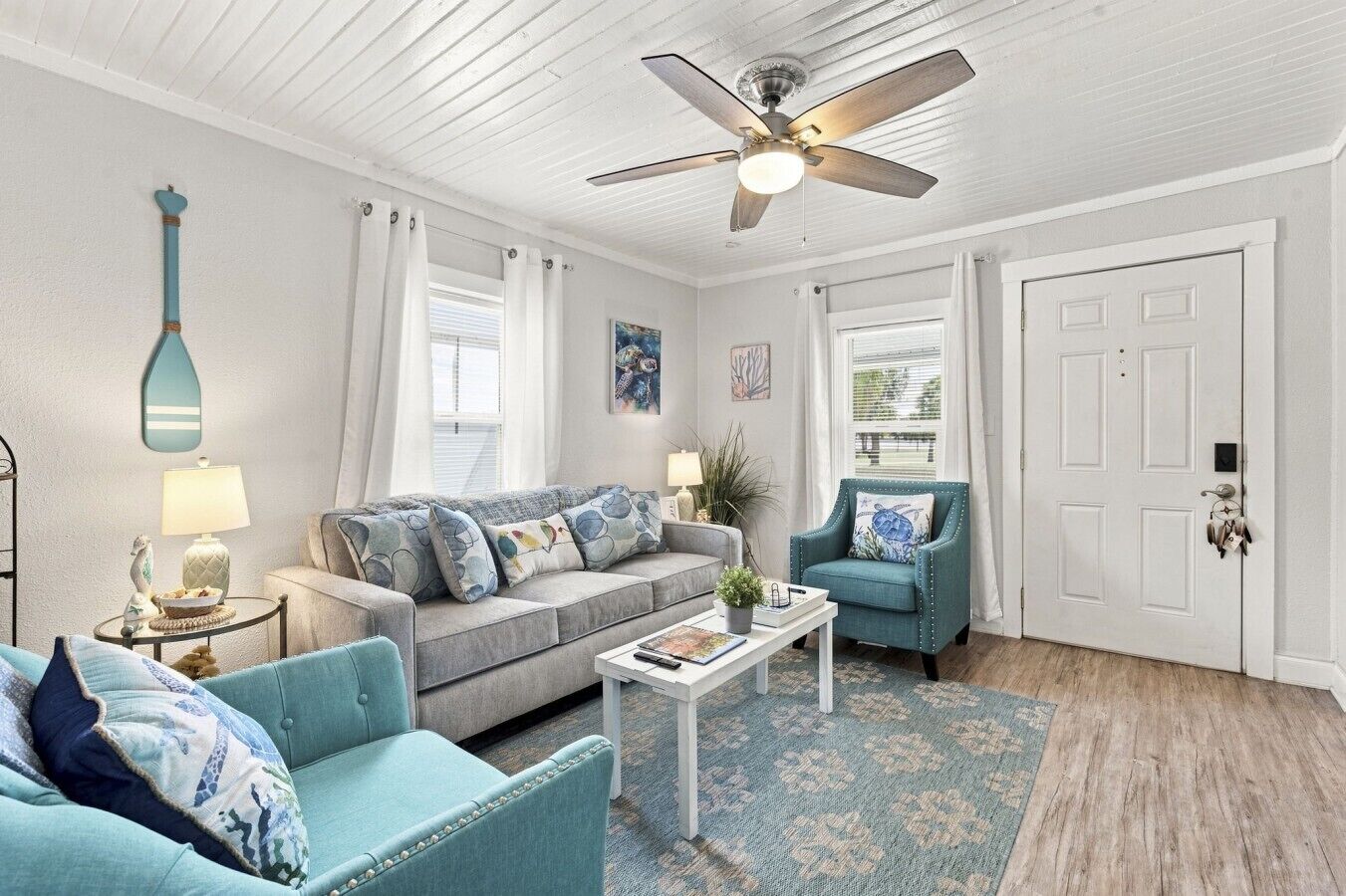 A living room with a ceiling fan, a sofa, a chair, a coffee table, and a door.