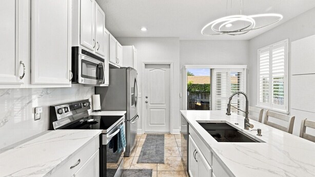 A modern kitchen with white cabinetry, stainless steel appliances, and a marble countertop. - 3 Bedroom House with Hot Tub Close to Downtown and Stadiums (Tampa)