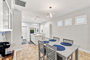 Eine moderne Küche mit weißen Schränken, einem Essbereich mit Tisch und Stühlen sowie einer sichtbaren Kücheninsel mit Spüle.